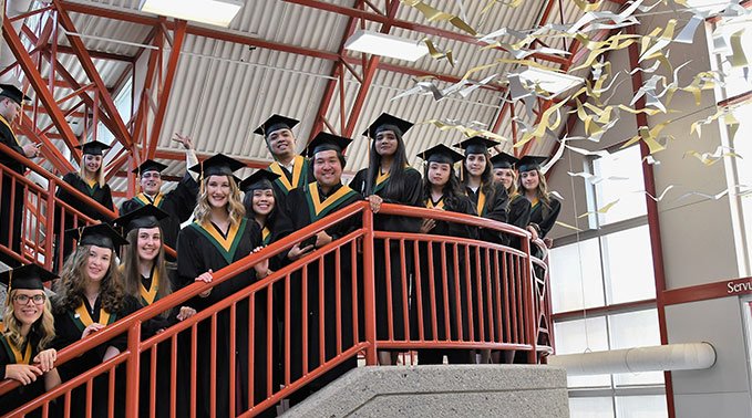 A group of graduating students smile down from a staircase at the Lloydminster campus.