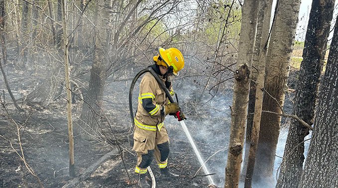 Student with hose sprays down smoldering forest floor