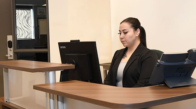 An administrative professional student types at a computer behind a desk.