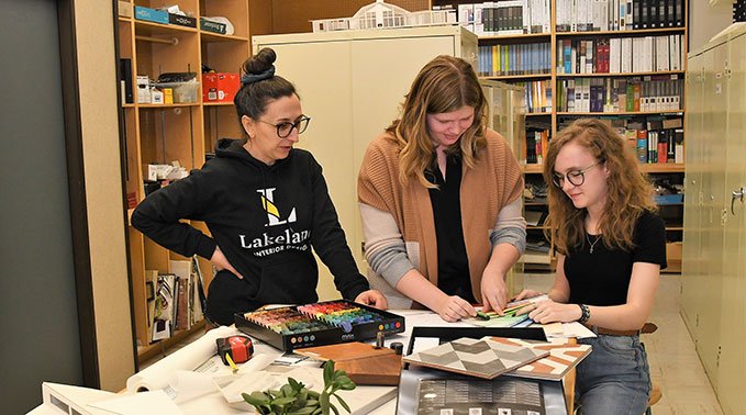 An interior design instructor and two students review swatches of fabric.