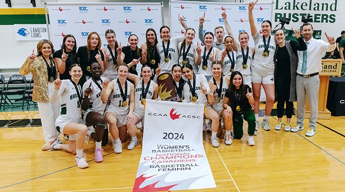 Lakeland Rustlers women's basketball team gather around thier championship banner.