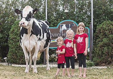 Three Lovich daughters with Holstein by farm sign
