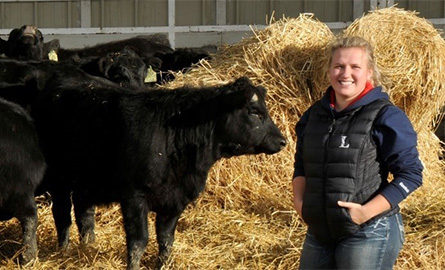 Student standing with cattle in a pen