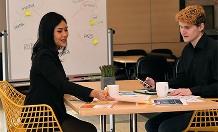 Two people discussing a marketing brief in front of whiteboard