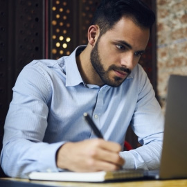 Student taking notes while working on a laptop
