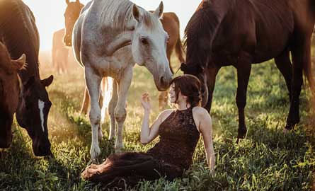 Woman sitting in field, surrounded by her horses
