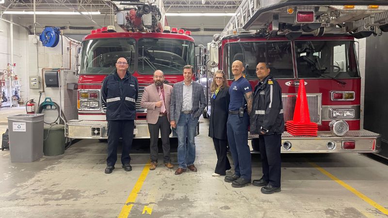 A group of people stand in front of fire trucks.