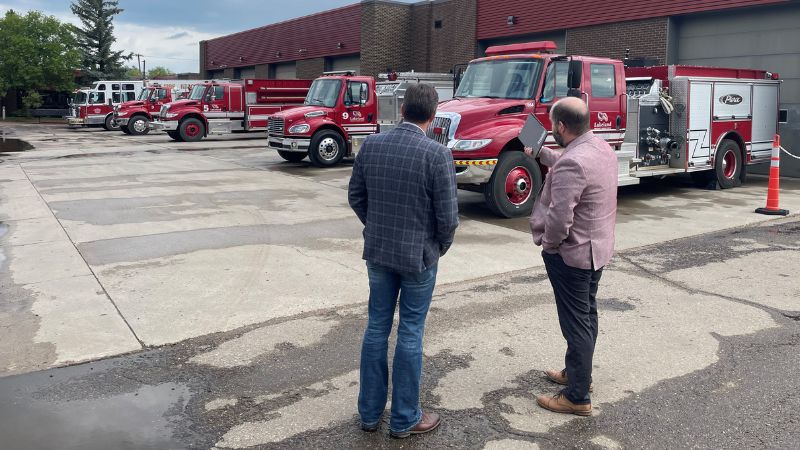Two people look at a row of fire trucks.