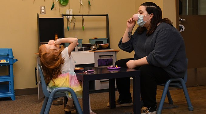 A human services student and a child play pretend drinking tea during the student-led play program.