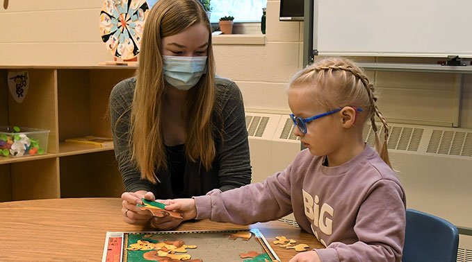 A early learning child care student helps a child finish a puzzle during the student-led play program.