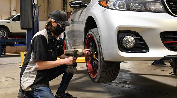 A automotive service technician student installs a tire to a hoisted car.