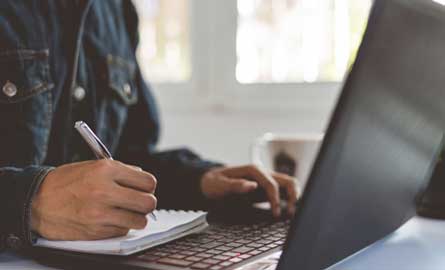 Student with notepad sitting in front of a laptop